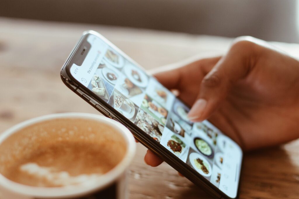 Food photos on a phone screen next to a cup of coffee
