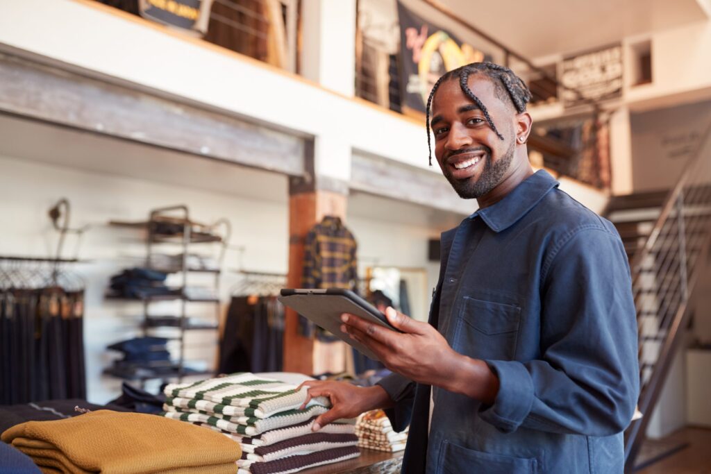 Retail clothing store owner holding a tablet and smiling.