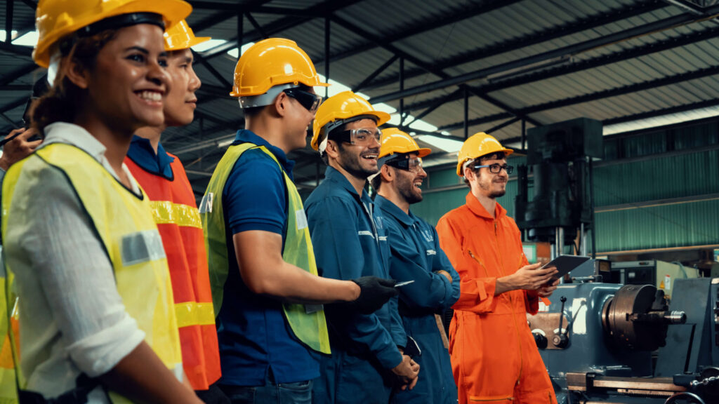 Warehouse workers in hardhats and vests standing together and laughing.