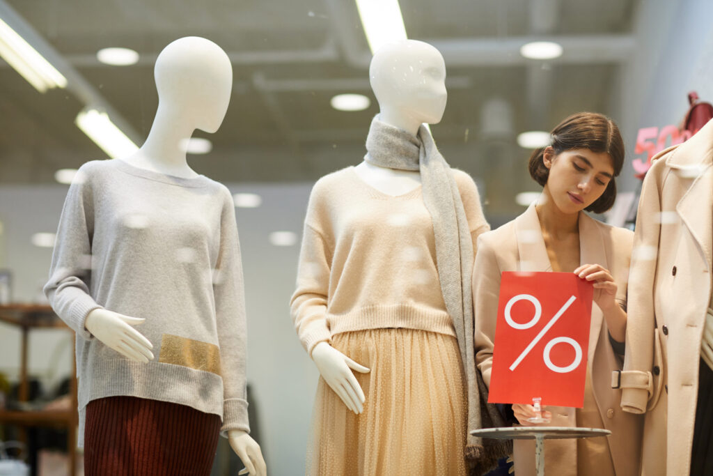 Retail employee setting up sale sign next to mannequins in a display