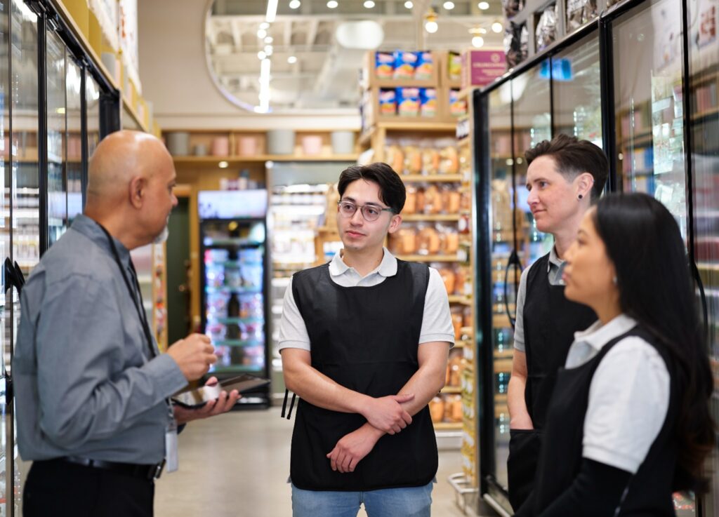 A manager in a grocery store speaks to a group three associates