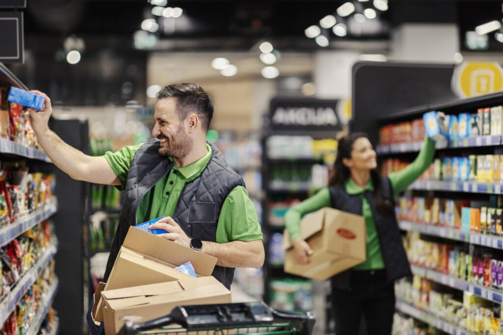 Happy employees putting groceries on shelves at supermarket.