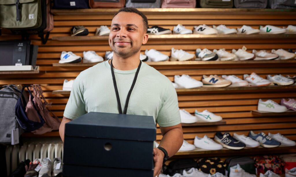 A male retail associate holds a shoe box while working during a new product launch.