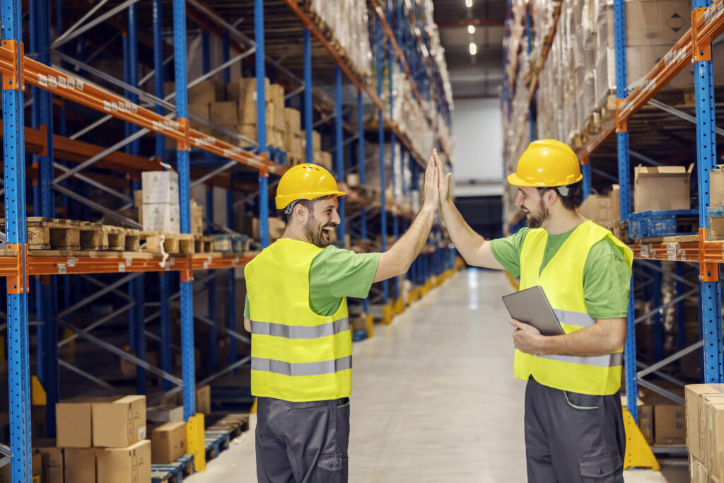 Two Warehouse Clerks Giving Each Other High Five For Teamwork In Import And Export Firm.