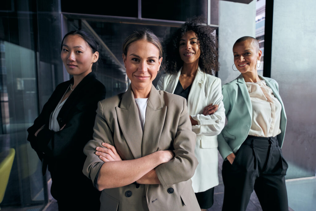 4 Professionally dressed women standing together and posing for picture