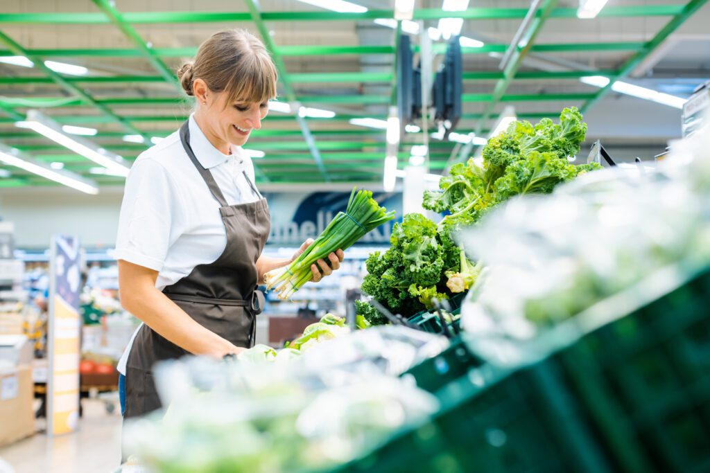 Shop Assistant In Supermarket Re Stocking Fresh Vegetables