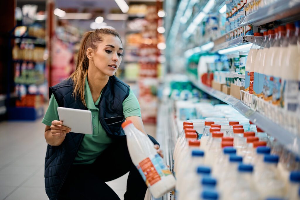 Female Supermarket Employee Arranging Products In Dairy Section.