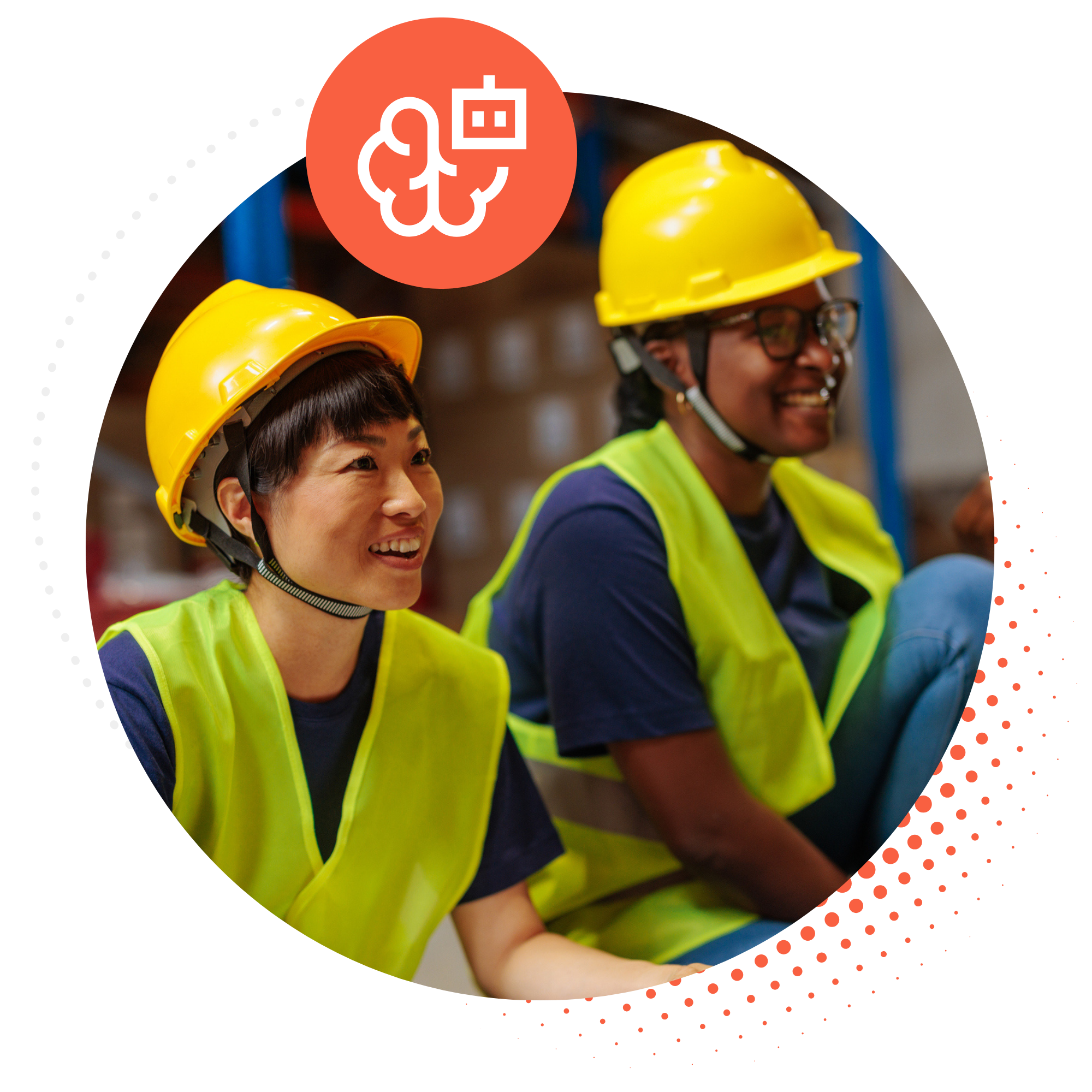 Two smiling warehouse workers in hard hats and hi‑vis vests sharing a light moment on the floor